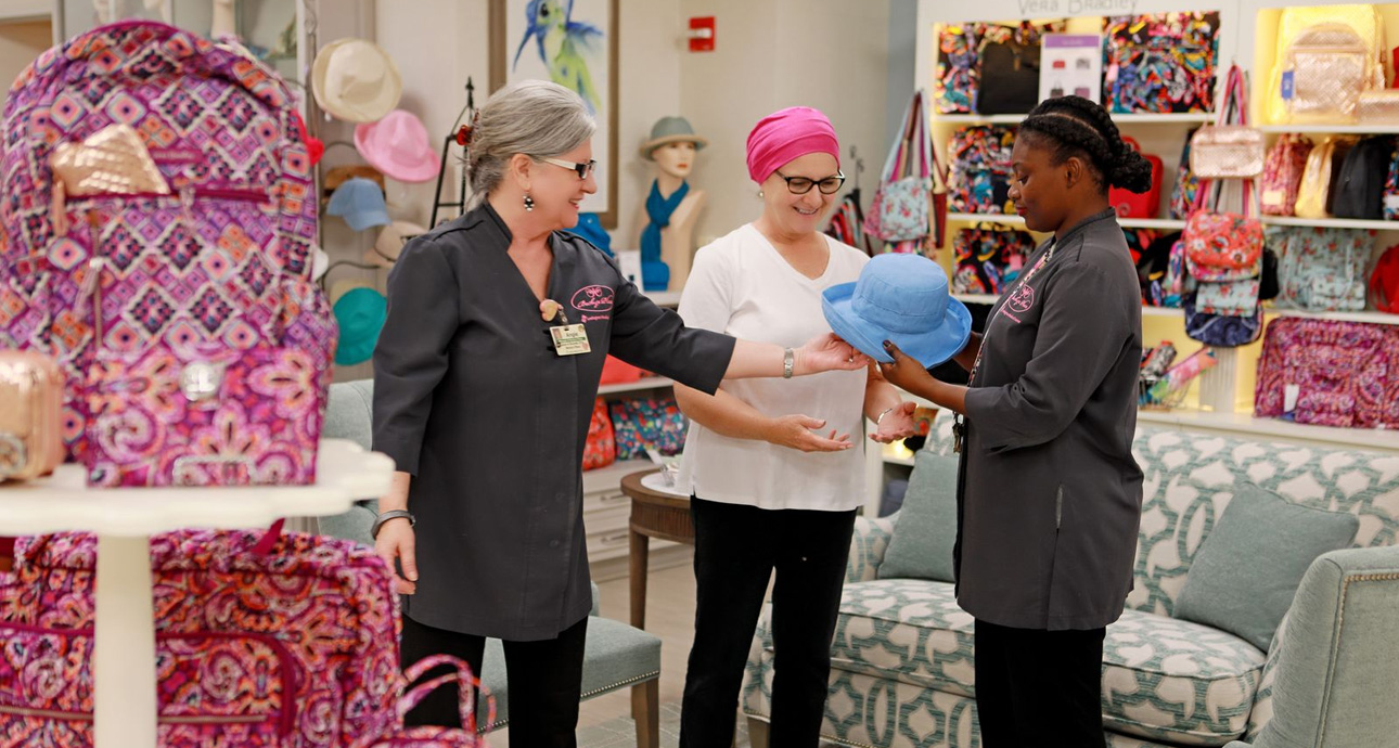 Smiling employees and a cancer patient looking at hats in a boutique that sells colorful bags, hats and accessories.