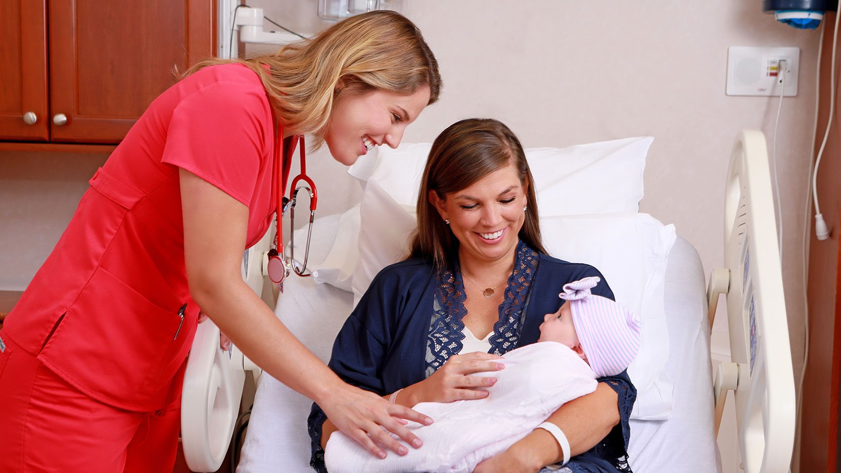 A nurse and woman holding and smiling at a baby.
